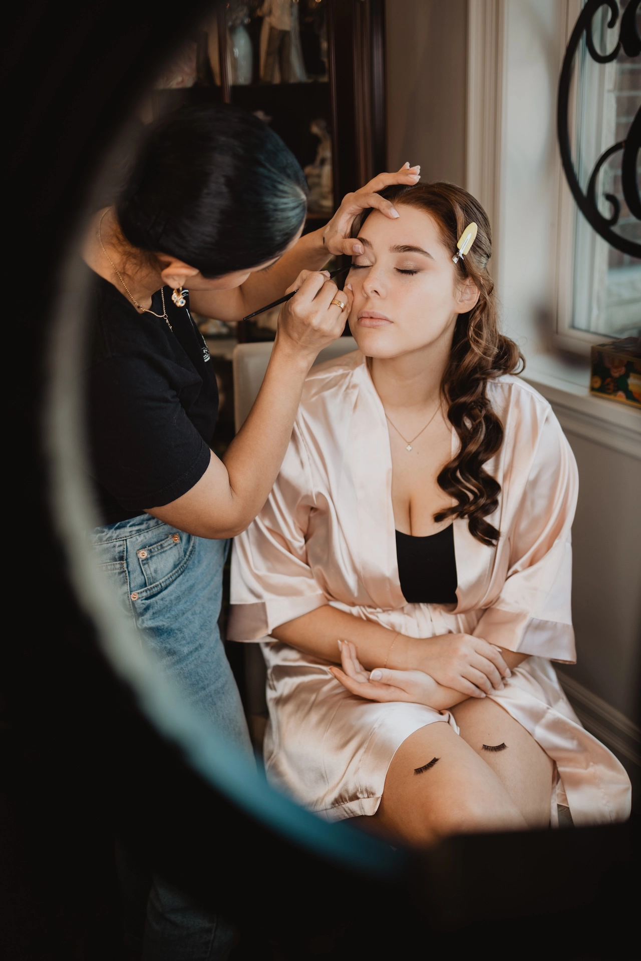 A serene moment of the bride captured in the mirror while having her makeup done in a silk robe. A timeless bridal preparation scene from Southern Ontario wedding photography.