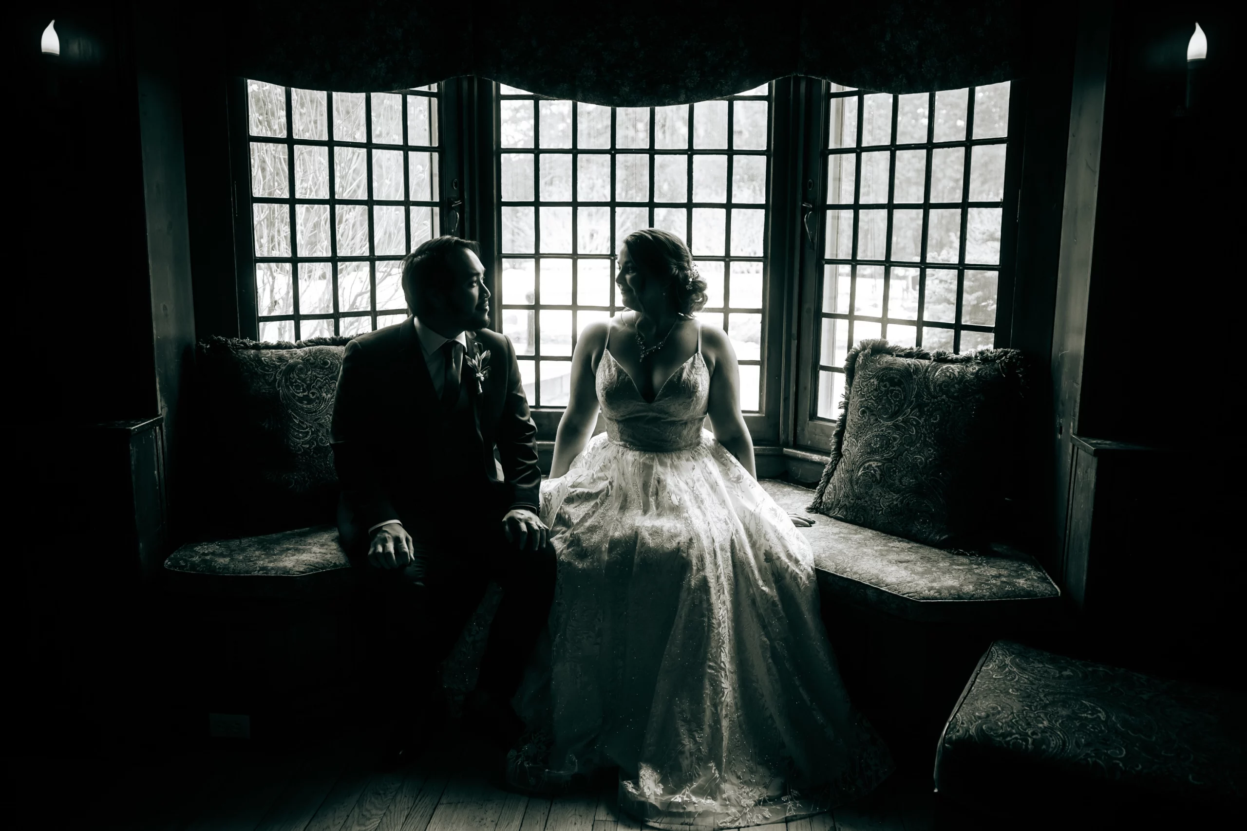 Dramatic black and white silhouette of the bride and groom sitting by a window, capturing the intimate and moody atmosphere of a fine art wedding.