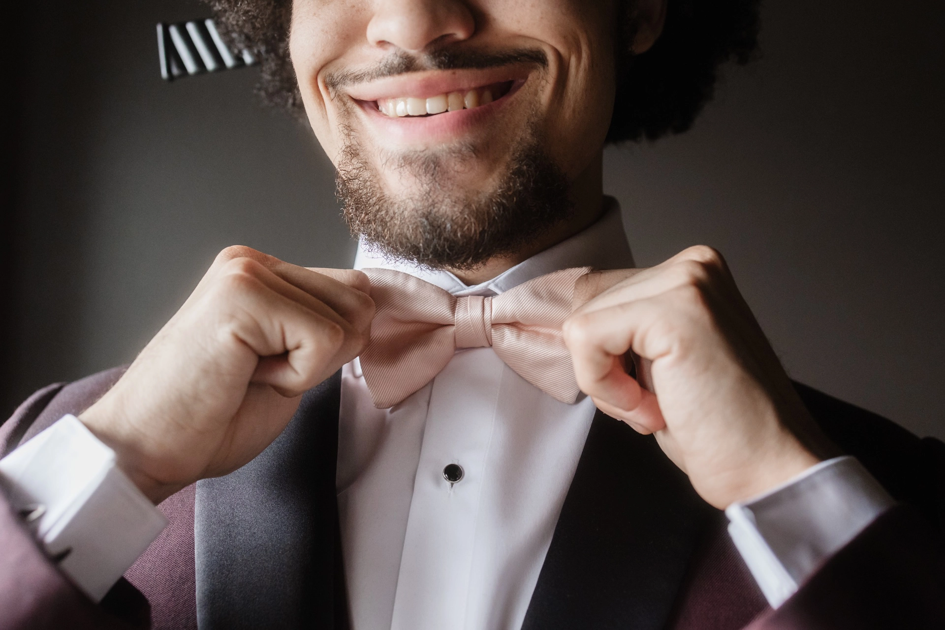 The groom smiles confidently while adjusting his bowtie, showcasing his stylish afro hair, captured during a wedding in Southern Ontario by Alissa Baltazar.