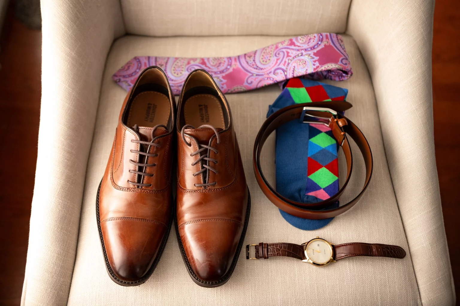 Flat lay of groom's accessories including watch, shoes and tie.
