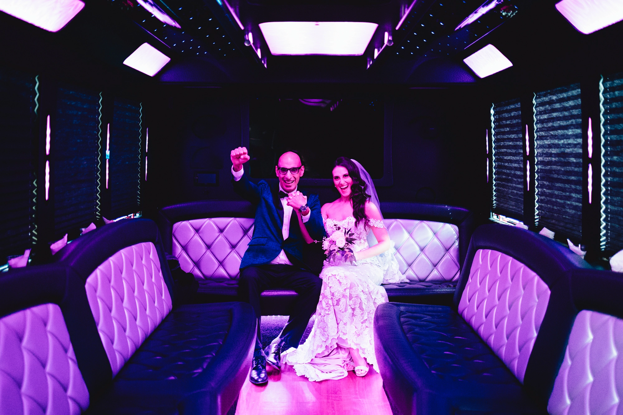 The newlyweds cheer with joy inside their wedding limo bus, soaking in the celebration.