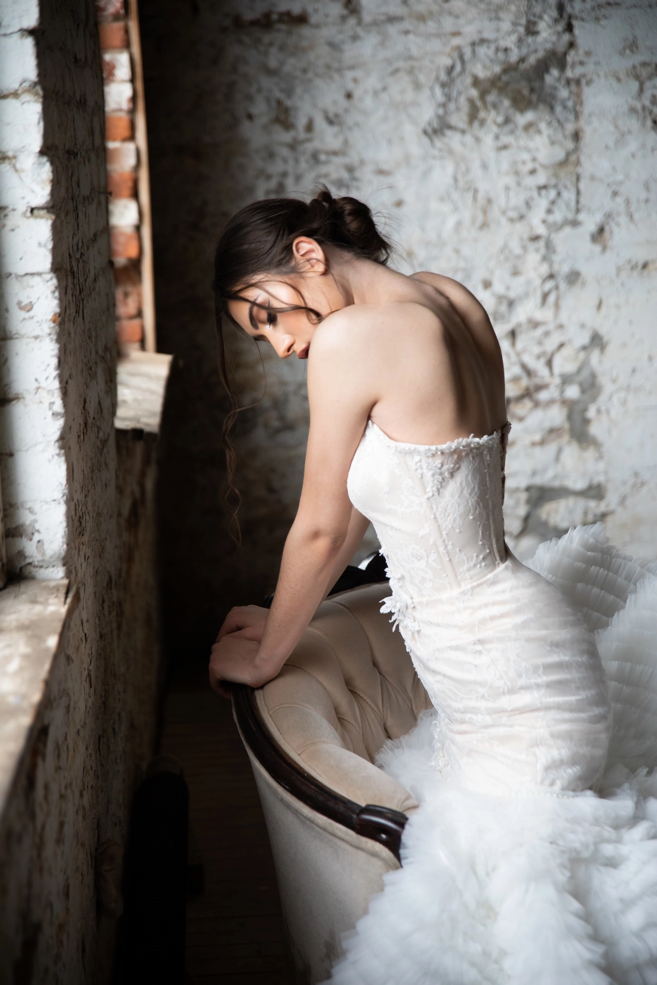 A fashionable bride lounges gracefully on a couch by the window, bathed in natural light.