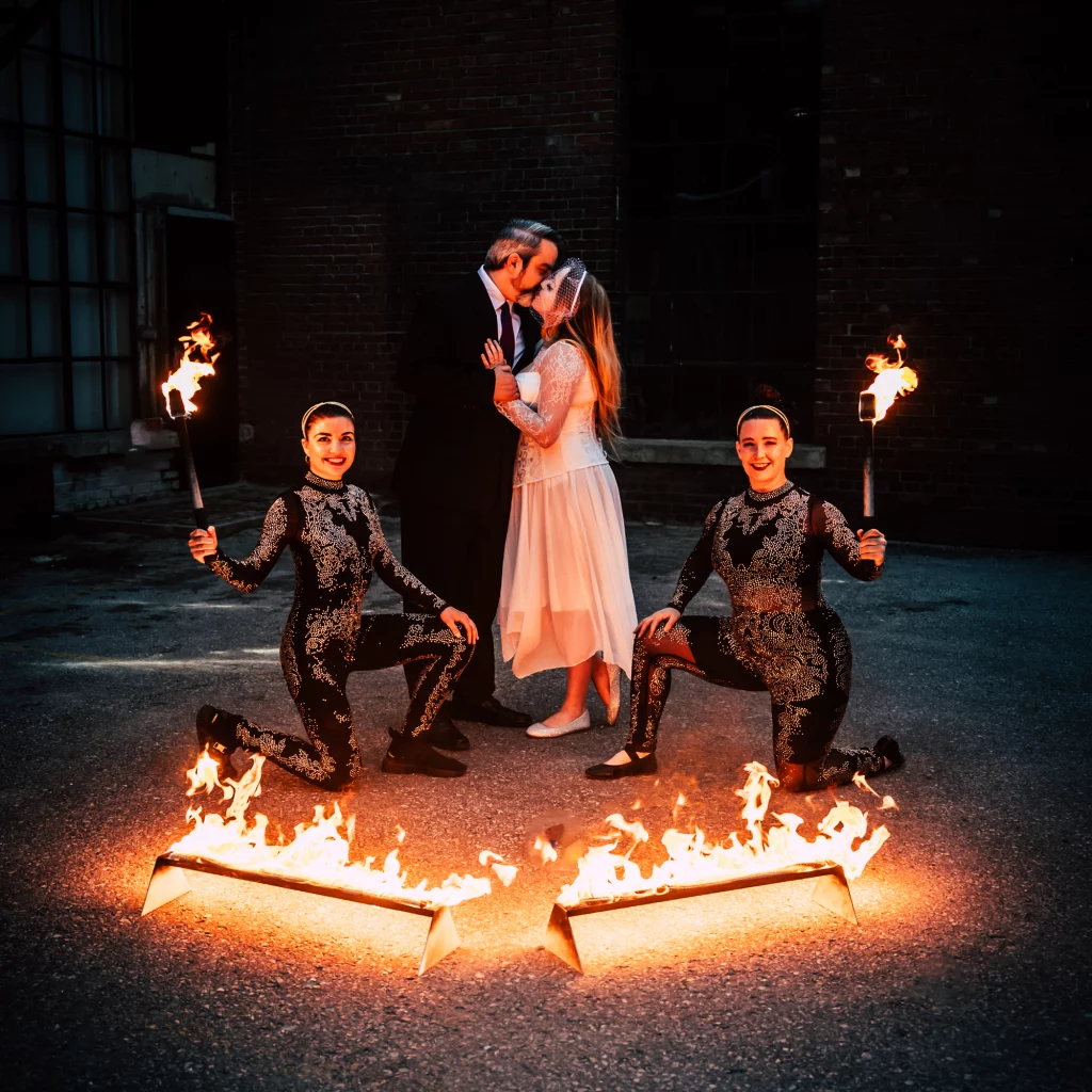 Bride and groom posing with Hoop You fire dancers during a fire show wedding performance