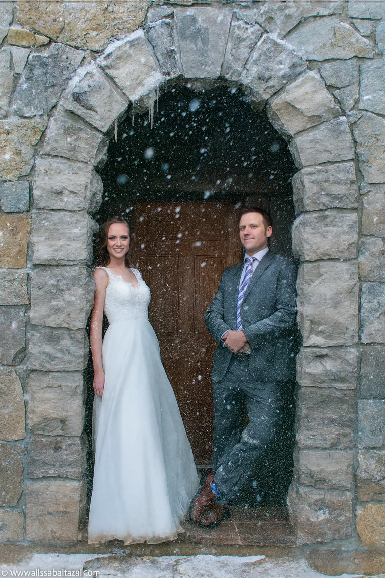 Wedding photographer photography capturing a couple under a snow-covered stone arch