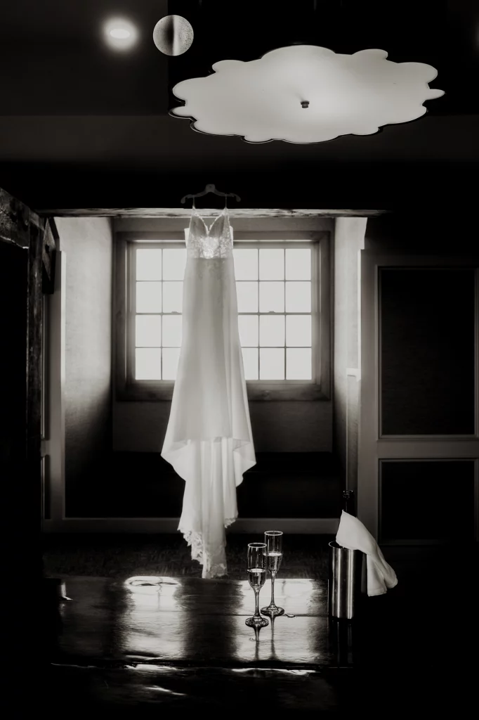 Black and white shot of the dress hanging on the window of Cambrige Mill's getting ready room.