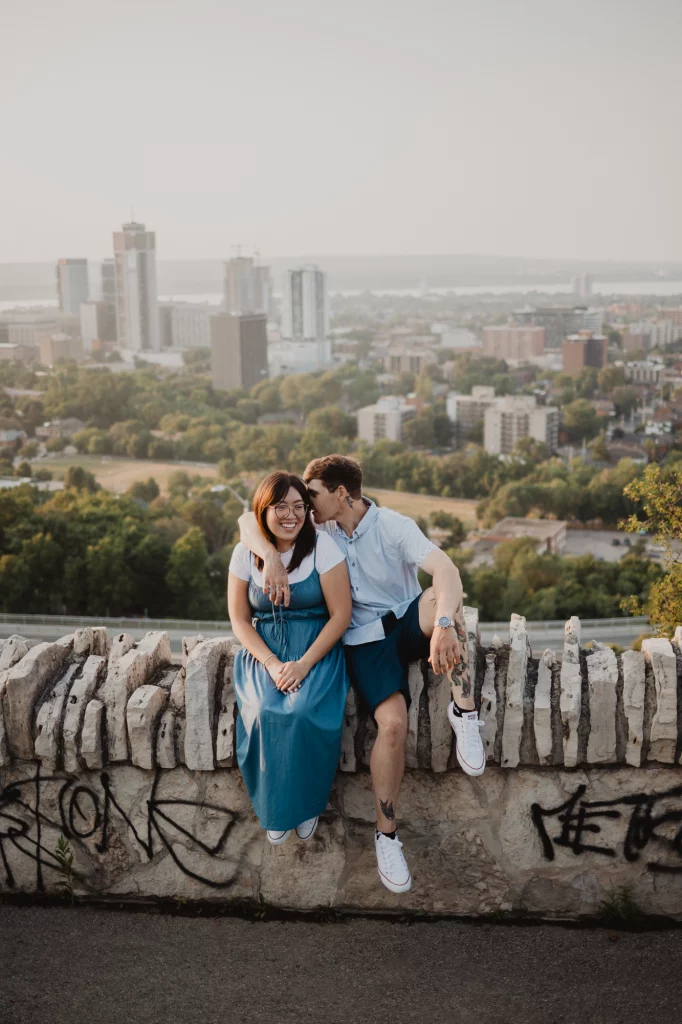 Couple snagaling sitting at the stone wall at the Sal laurance park Hamilton, dresses stylish.
