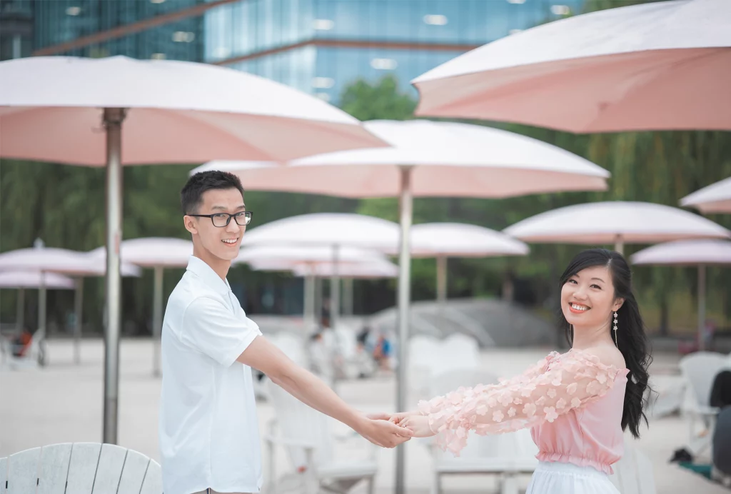 Beautiful asian couple holding hands infront of pink beach umbrellas downtown Toronto.